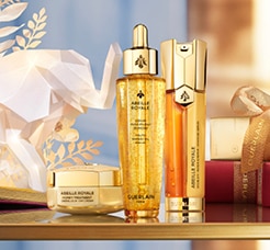 Guerlain Abeille Royale luxus bőrápoló termékek arany csomagolásban, elegáns ünnepi háttérrel.